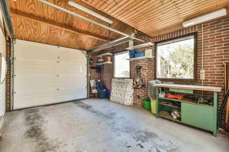 Garage built of brick and with concrete screed. There is overhead lighting and several fixtures and fittings. The garage is closed with a white gate that lowers from the top.