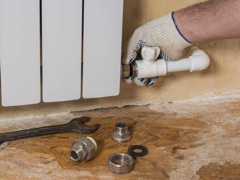 Repairing a radiator that leaks. You can see the components for fixing the hot water supply pipe to the radiator. A spanner and various fittings for the radiator lie beneath the radiator.