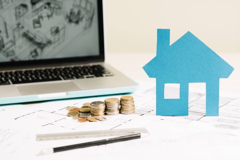 The graphic illustrates the cost of the house extension. It shows a dozen coins arranged in mounds, a blue house and in the background on a laptop you can see an architectural plan of the building.